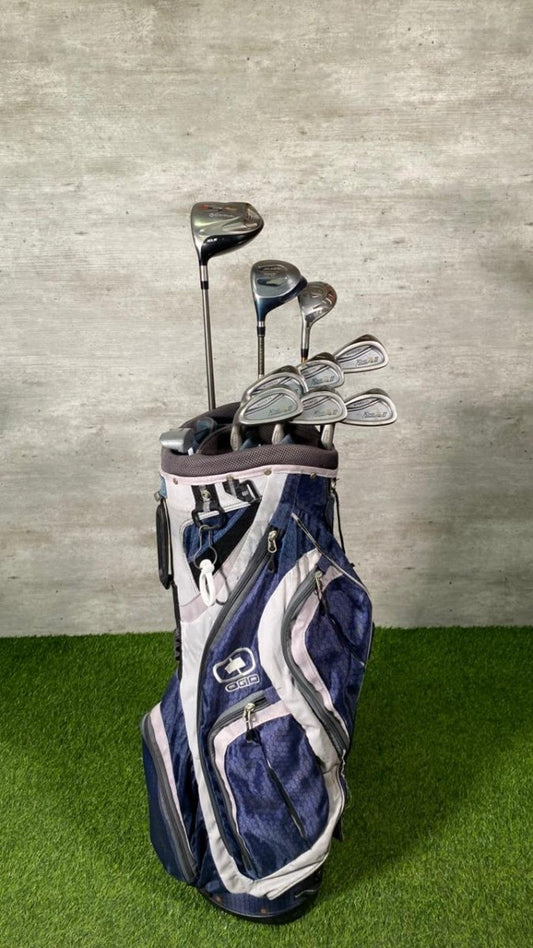 Golf clubs in a blue and white bag on a grassy surface with a concrete wall background