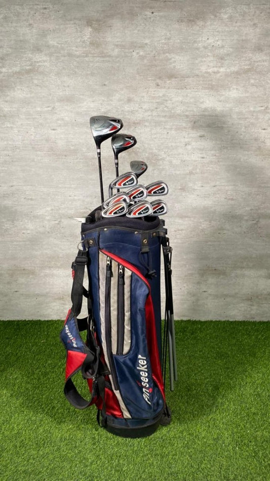 Golf clubs in a bag on a grassy surface with a concrete wall background