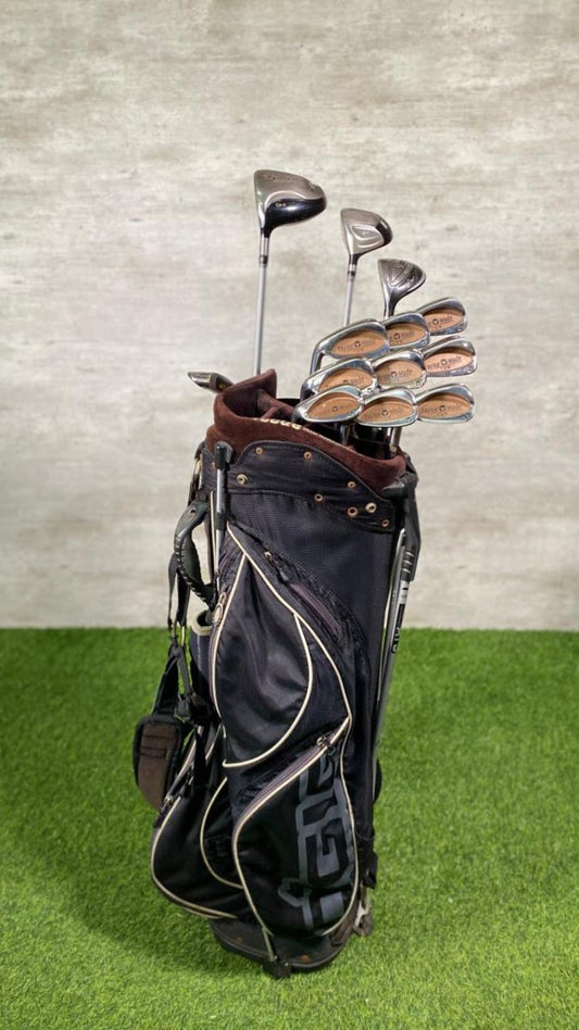 Golf clubs in a black bag on green grass with a gray wall background