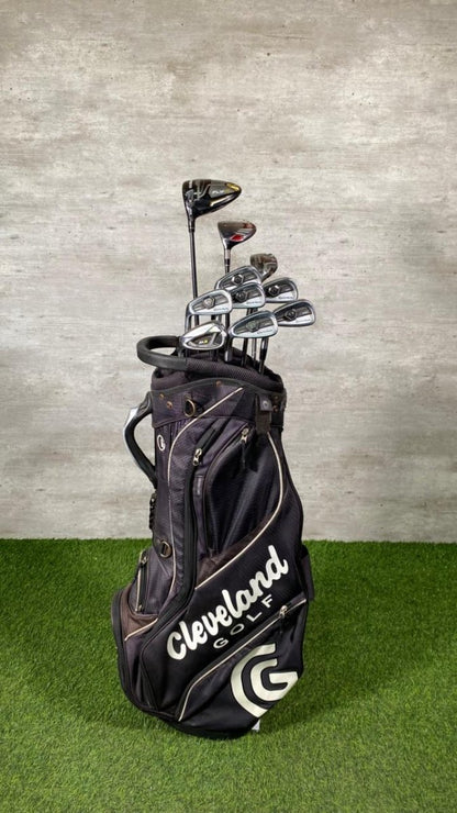 Golf clubs in a Cleveland Golf bag on a green surface with a gray concrete wall background