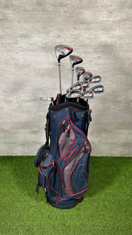 Golf clubs in a blue bag on grass with a gray wall background