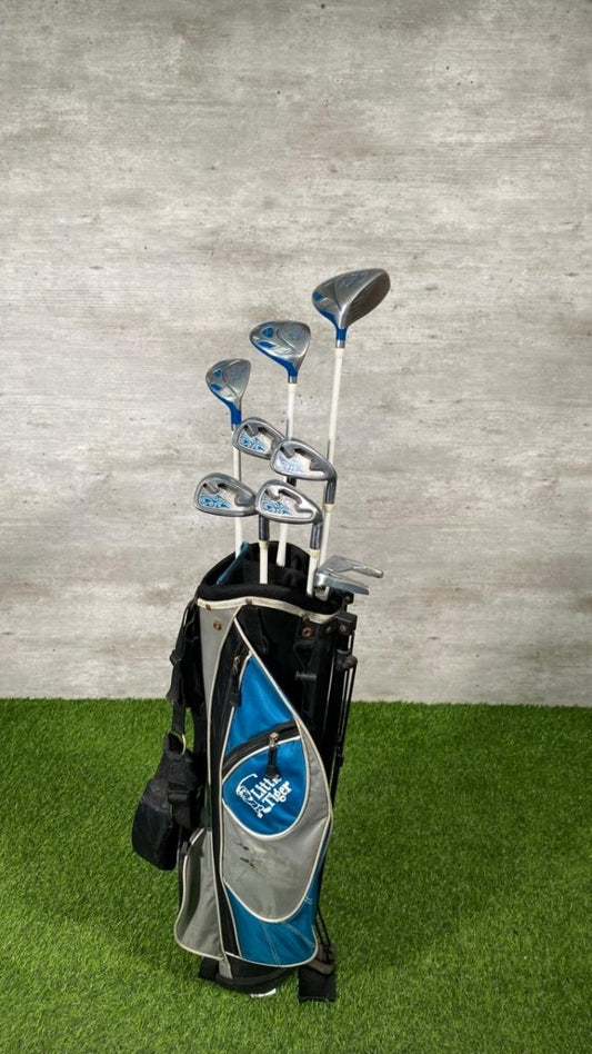 Set of golf clubs in a bag on a green surface with a gray wall background