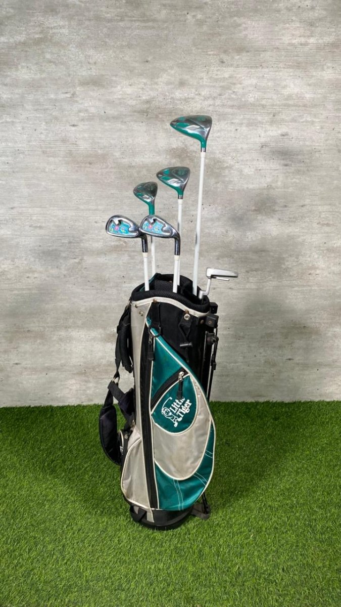 Golf clubs in a bag on a green surface with a gray wall background