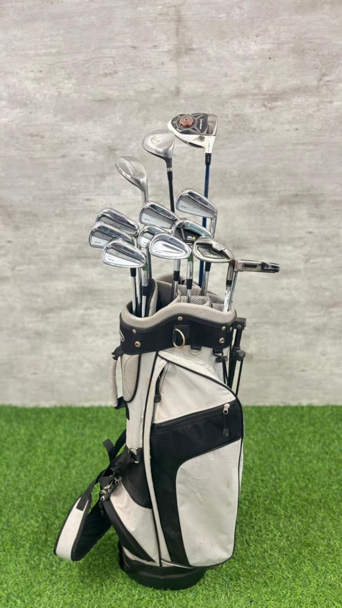 Set of golf clubs in a white and black bag on a grassy surface with a gray concrete wall in the background.
