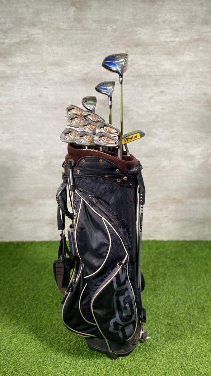 Golf bag with clubs on a grassy surface against a textured wall