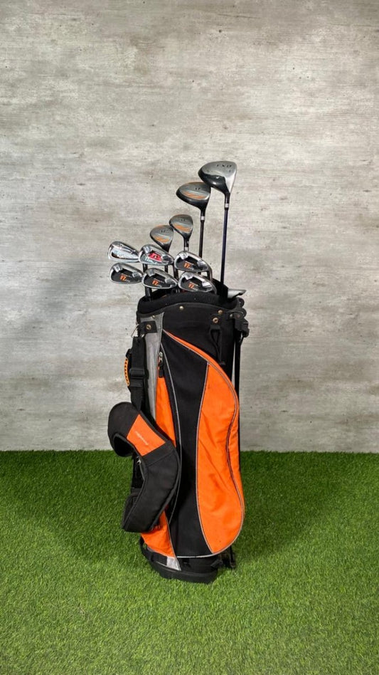Golf clubs in an orange and black bag on a green surface with a gray wall background