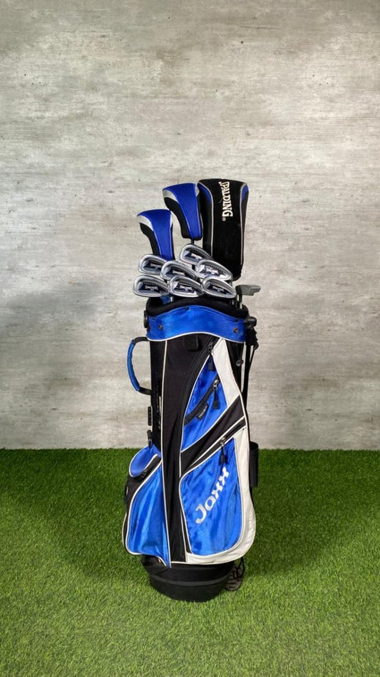 Golf club set in a blue and black bag on grass with a gray wall background