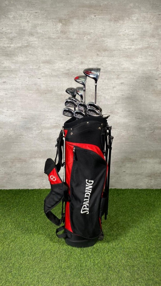 Golf clubs in a black and red bag on a grassy surface with a concrete wall background