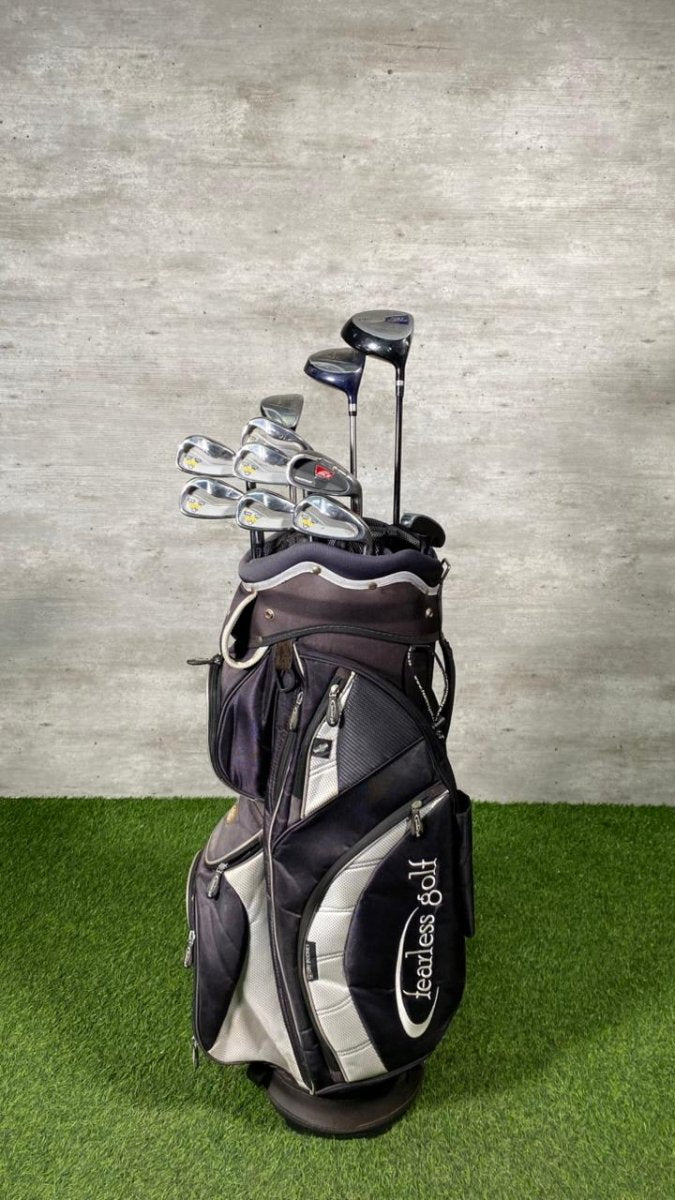 Golf clubs in a black and gray bag on a green surface with a gray wall background