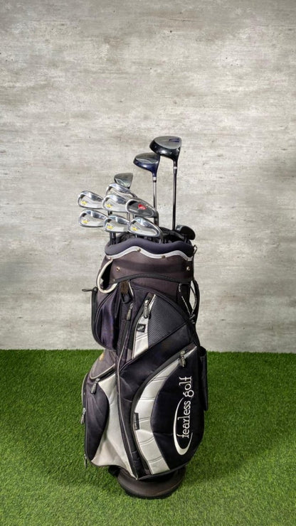 Golf clubs in a black and gray bag on a green surface with a gray wall background