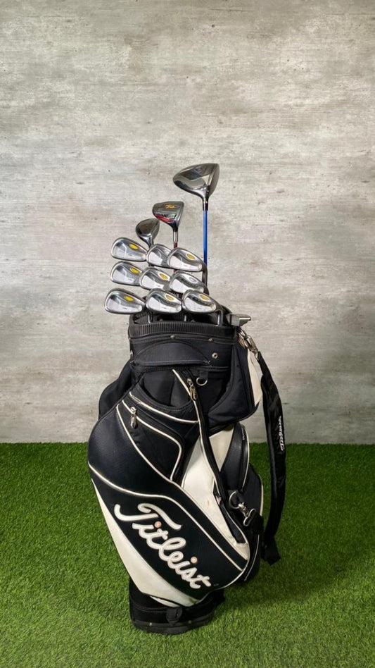 Golf clubs in a Titleist bag on a grassy surface with a concrete wall background