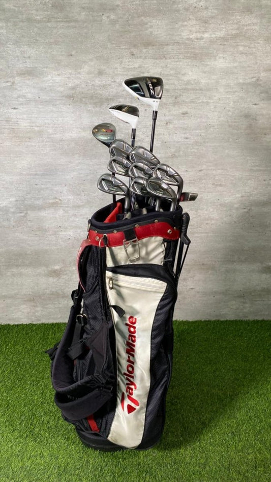 Golf clubs in a TaylorMade bag on a grassy surface with a concrete wall background