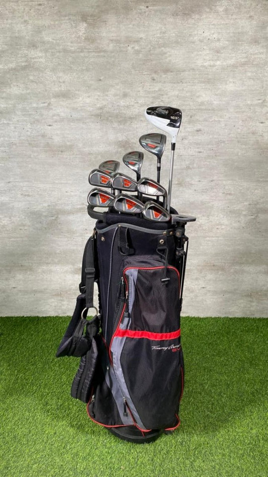 Set of golf clubs in a black bag on a grassy surface with a gray concrete wall background