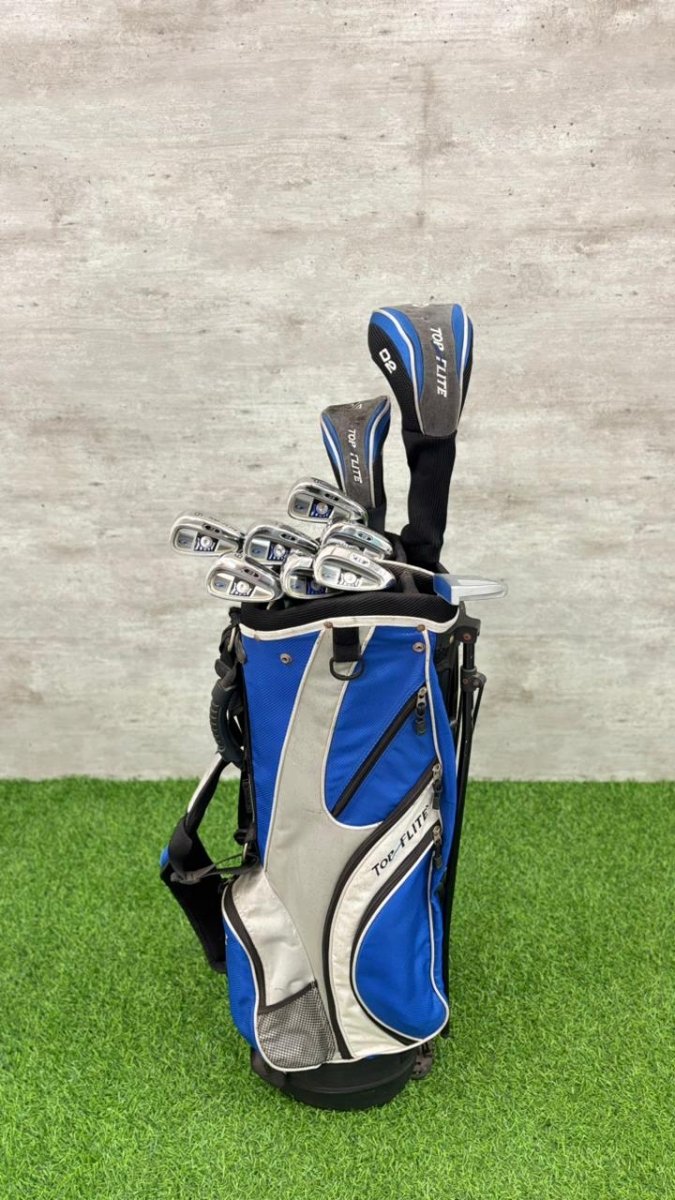 Golf clubs in a blue and gray bag on green grass with a gray wall background