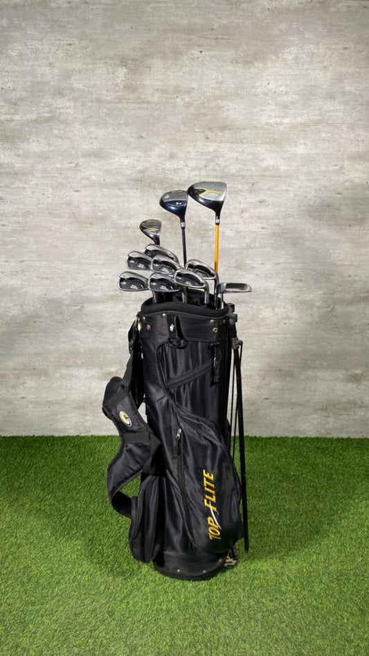 Set of golf clubs in a black bag on a grassy surface with a gray concrete wall background