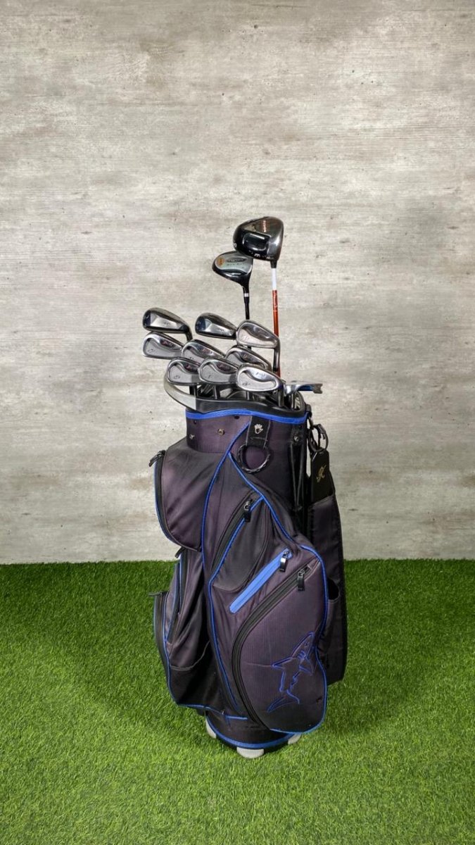 Golf bag with clubs on a grassy surface against a concrete wall