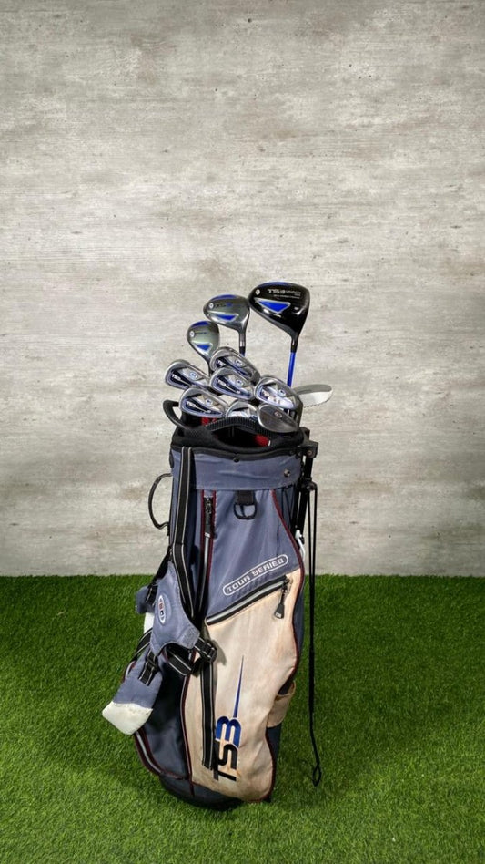 Golf bag with clubs on a grassy surface against a concrete wall