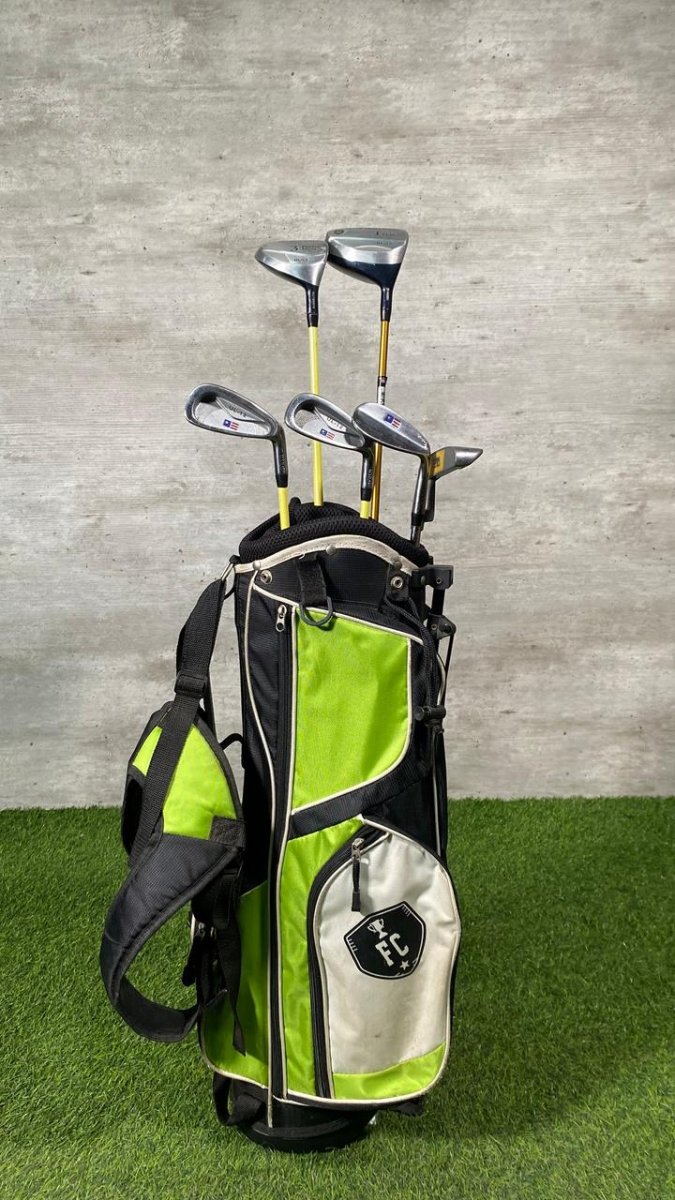 Green and black golf bag with golf clubs against a gray wall.