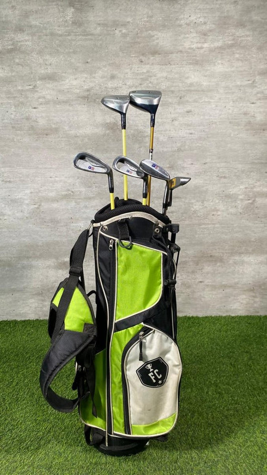 Green and black golf bag with golf clubs against a gray wall.