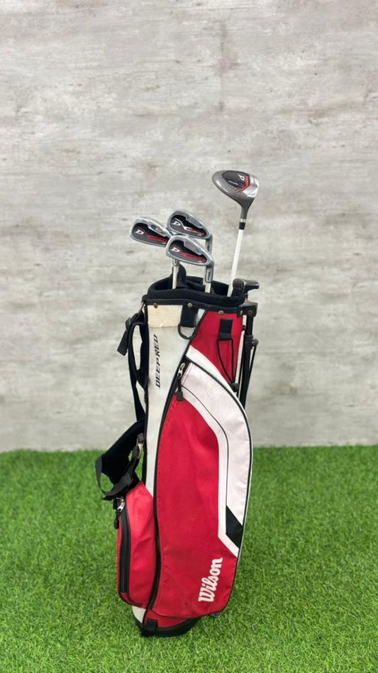 Golf clubs in a red bag on a grassy surface with a gray concrete wall background