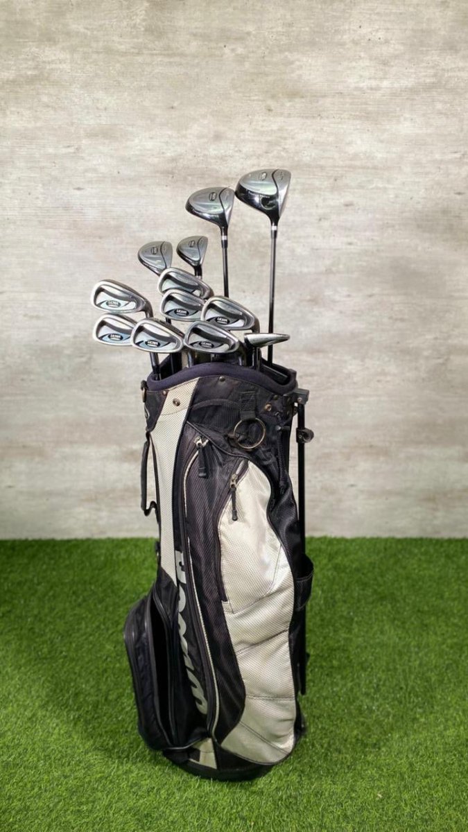 Golf clubs in a black and white bag on a green surface with a gray textured wall background