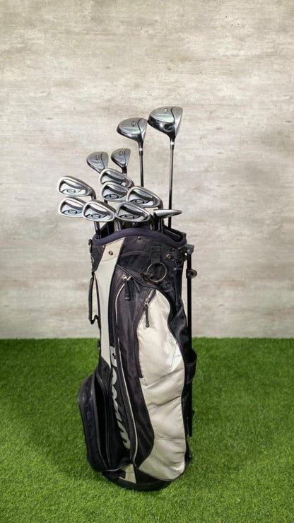 Golf clubs in a black and white bag on a green surface with a gray textured wall background