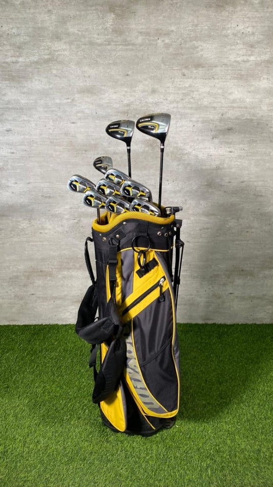Golf clubs in a black and yellow bag on a grassy surface with a concrete wall background